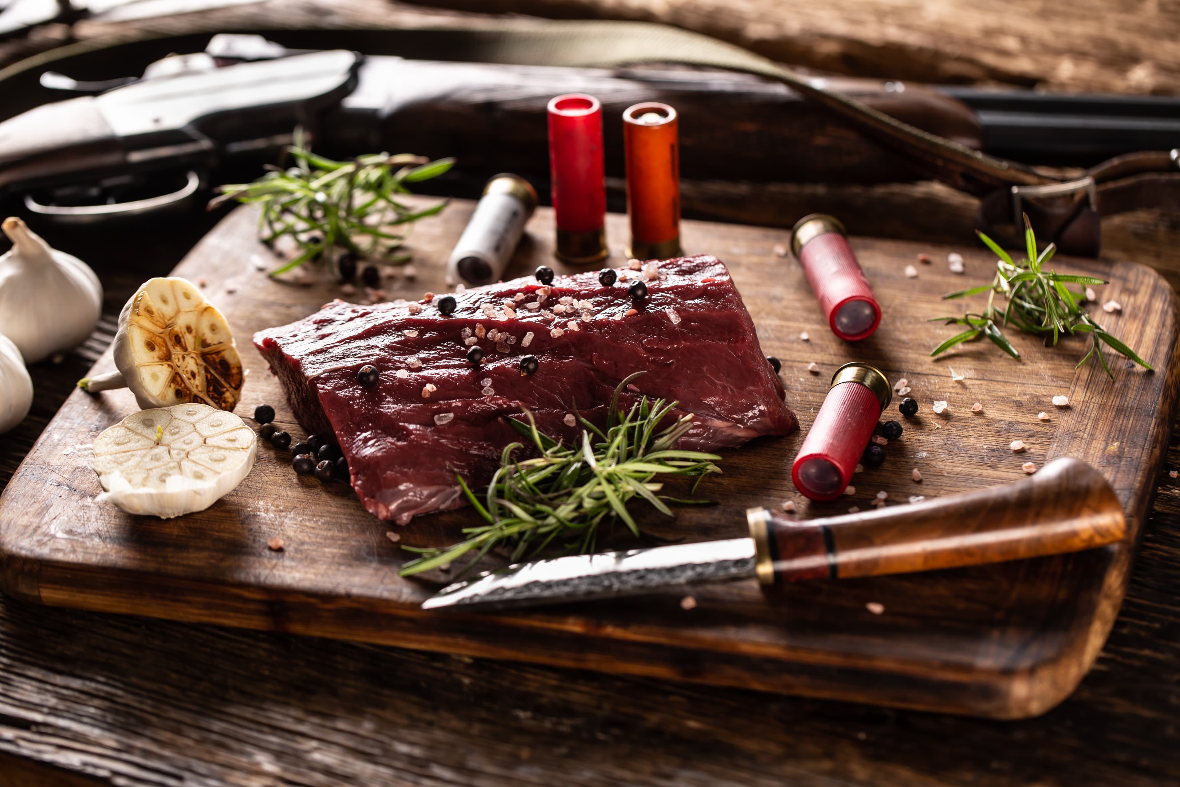 A venison loin on a wooden board with rosemary and garlic.