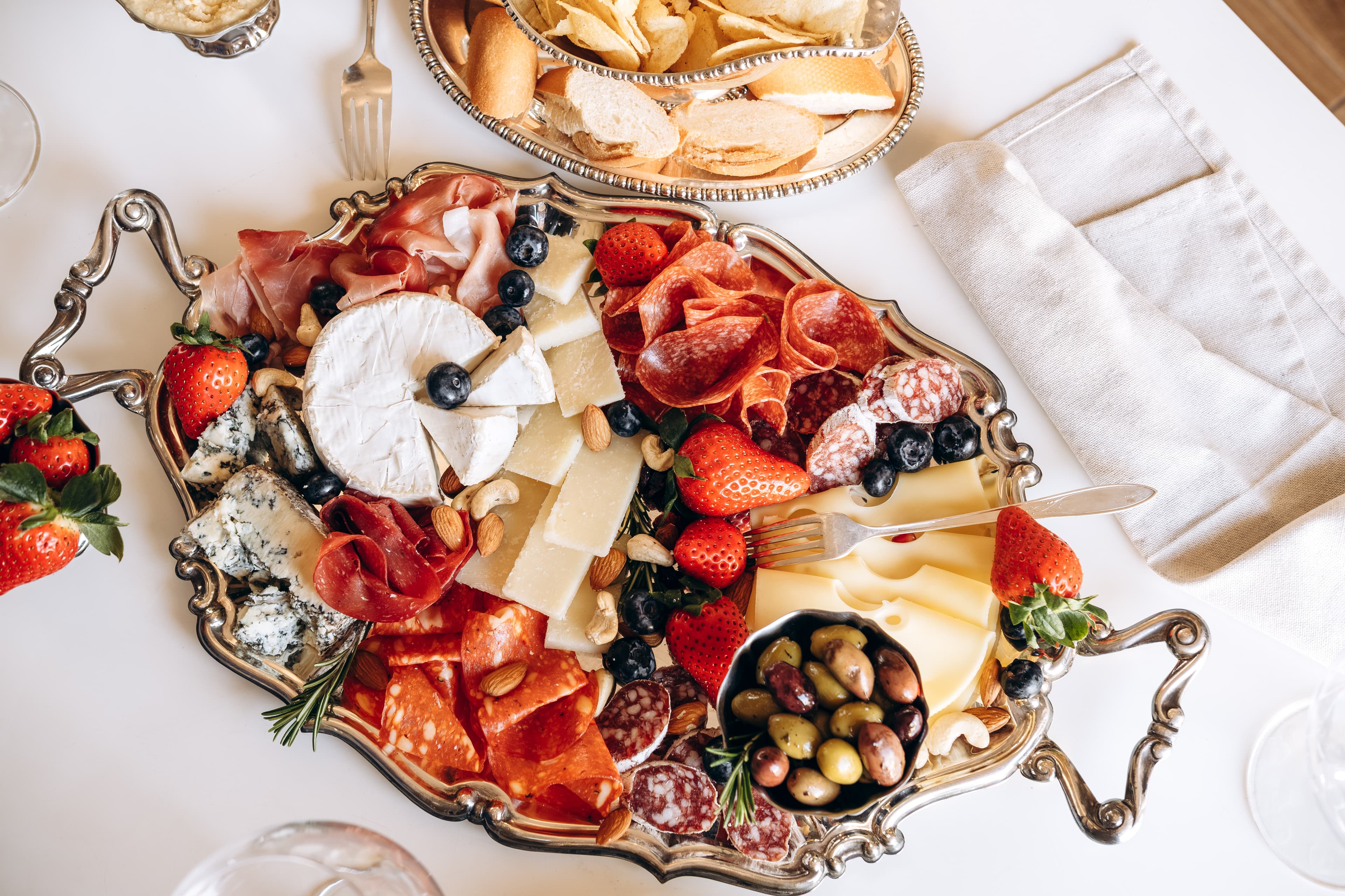 A silver tray of cheeses, cured meats, olives, and fruit.