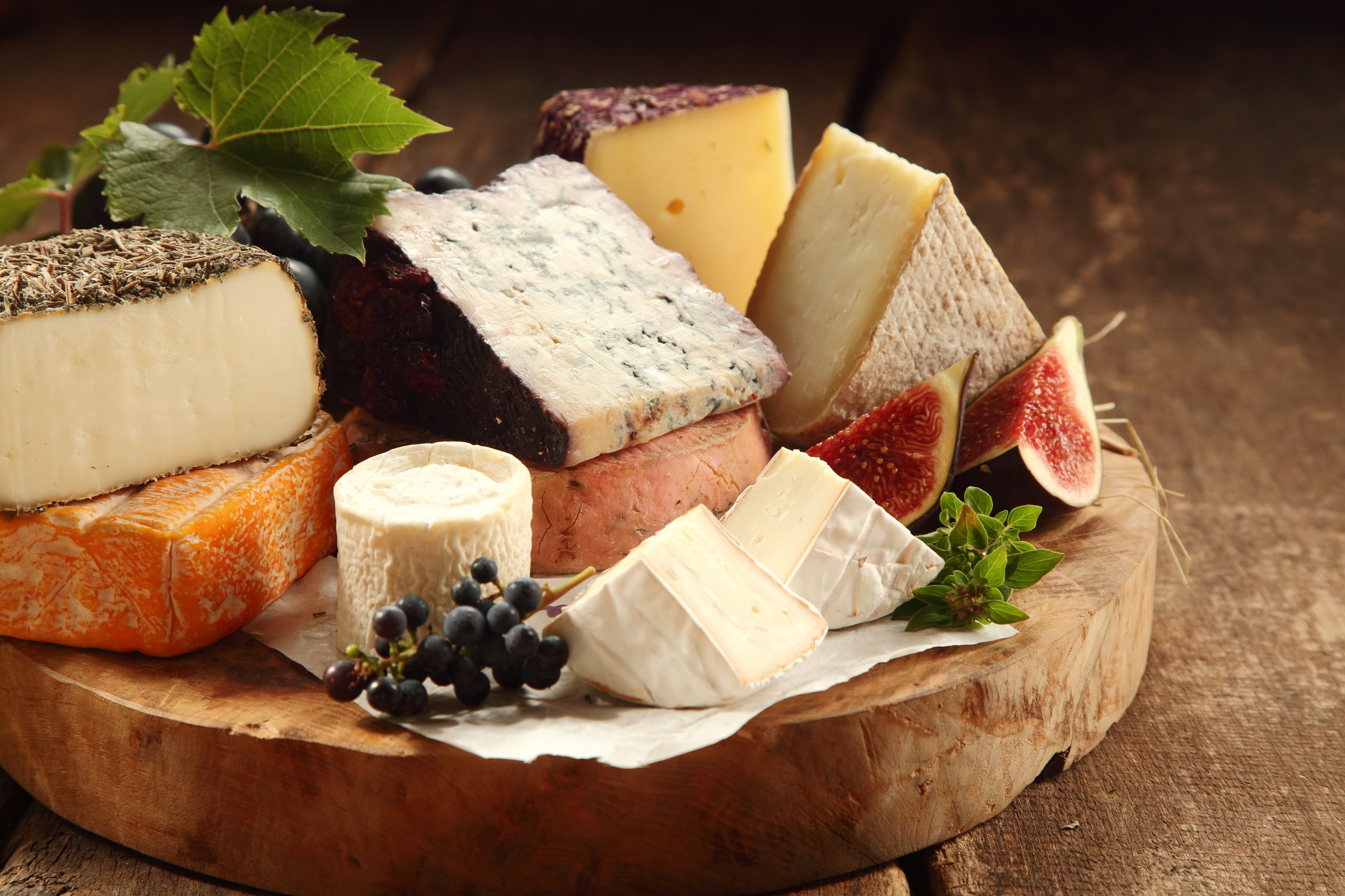 Artisan cheeses with figs and dark grapes on a wooden board.