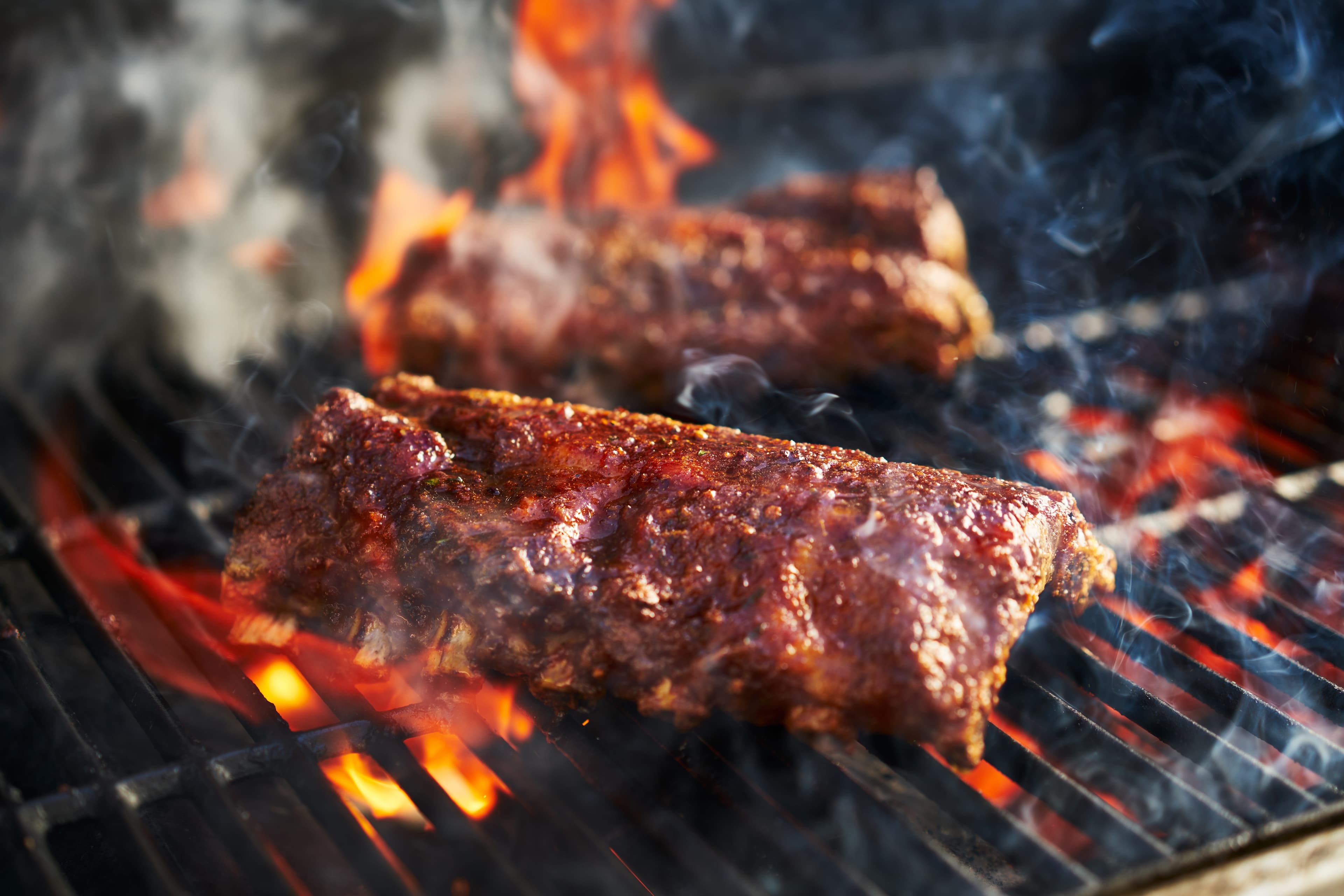 Pork ribs cooking over an open grill with smoke and flame.