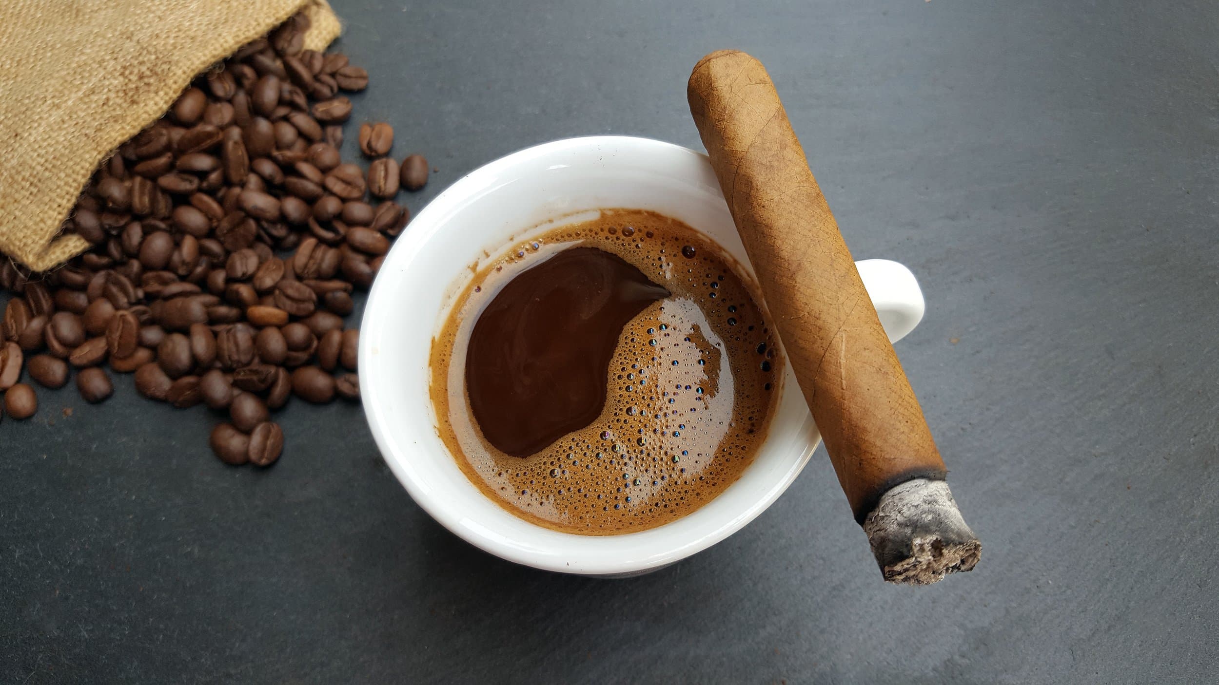 Cigar resting across a coffee cup with roasted beans.