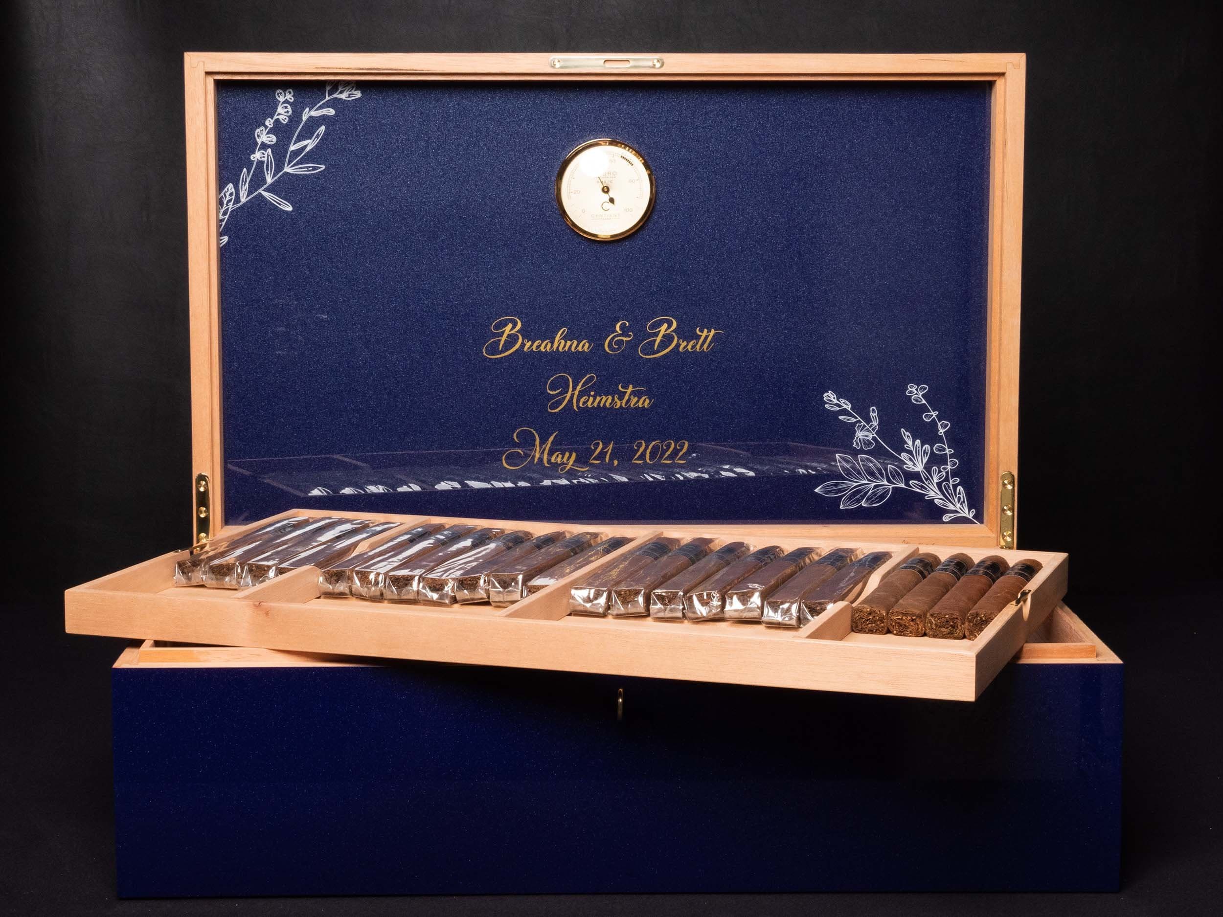 An open personalized navy Centient humidor with floral lid artwork and cigars arranged in its tray