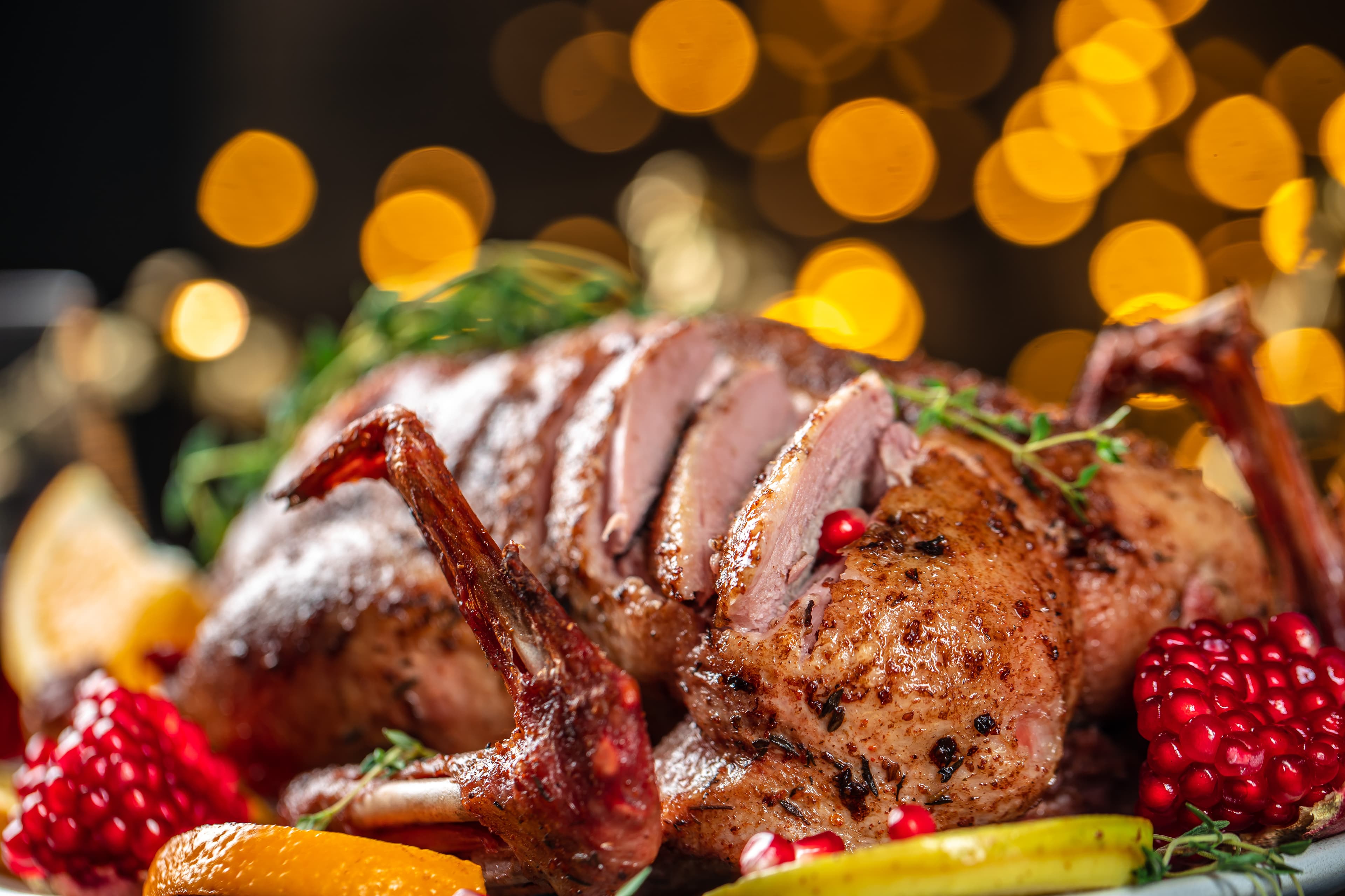 Sliced roast duck breast with fruit and herbs on a dark plate.