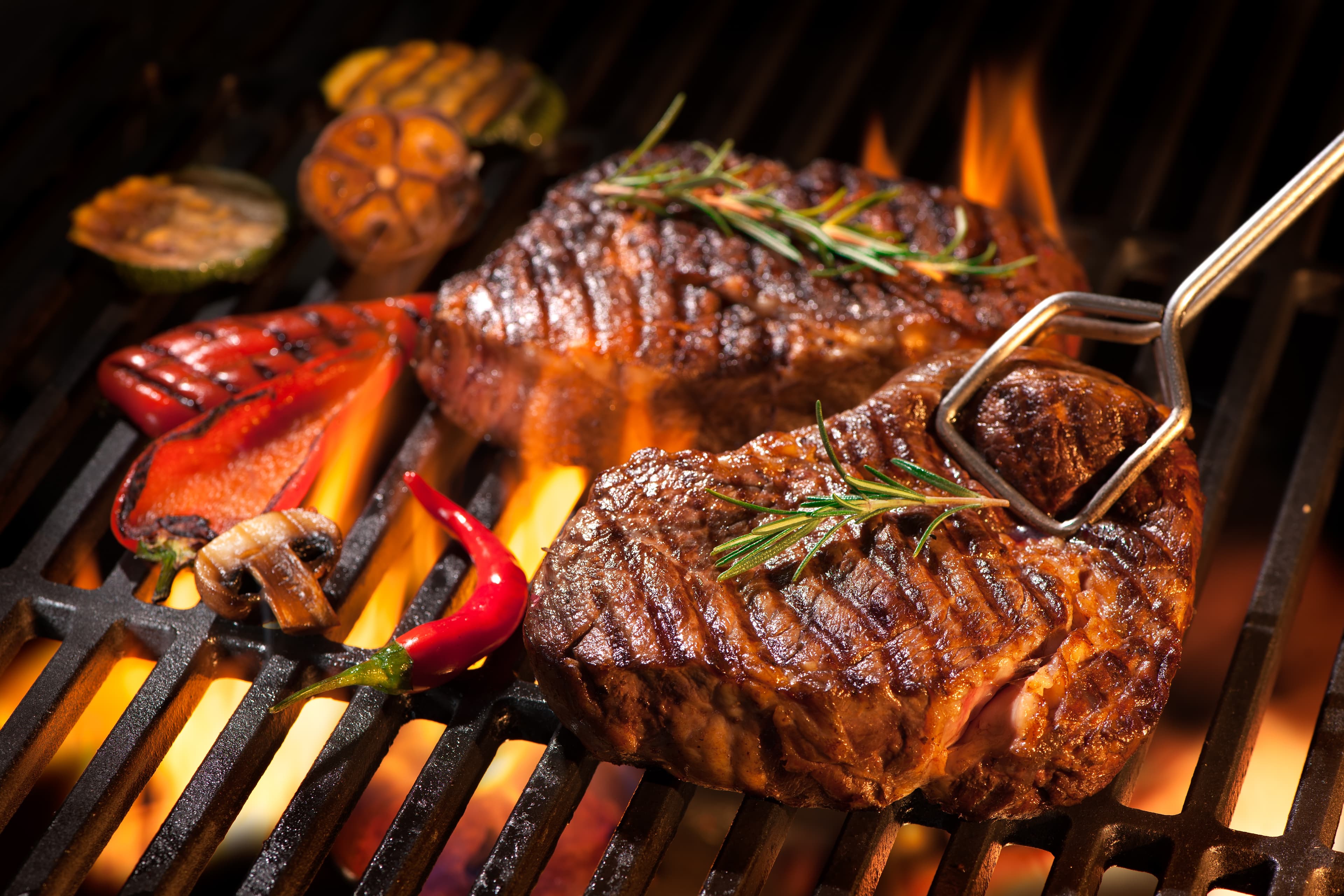 Beef steaks searing on a grill over open flame.