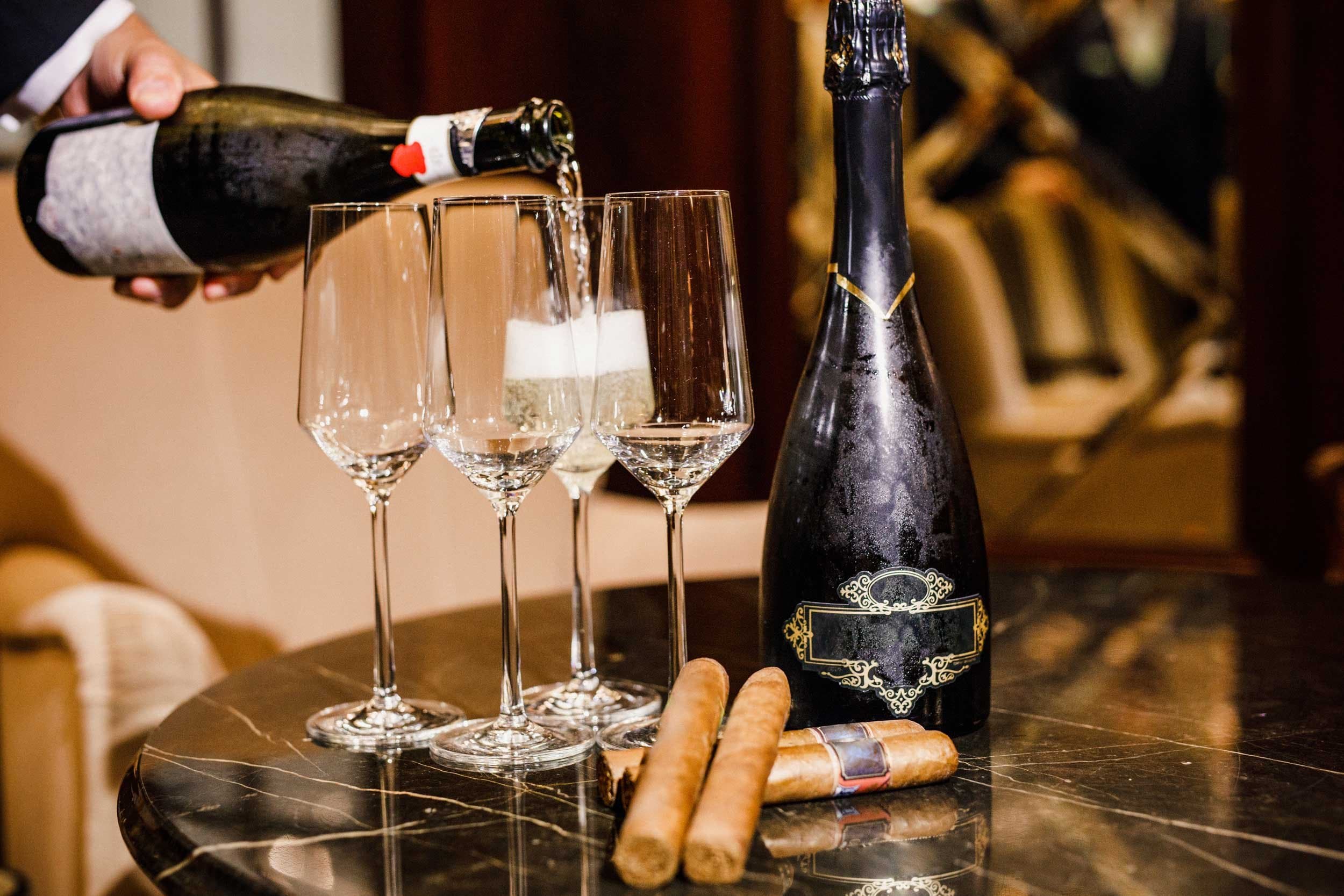 Sparkling wine poured into flutes beside cigars on a dark marble table.