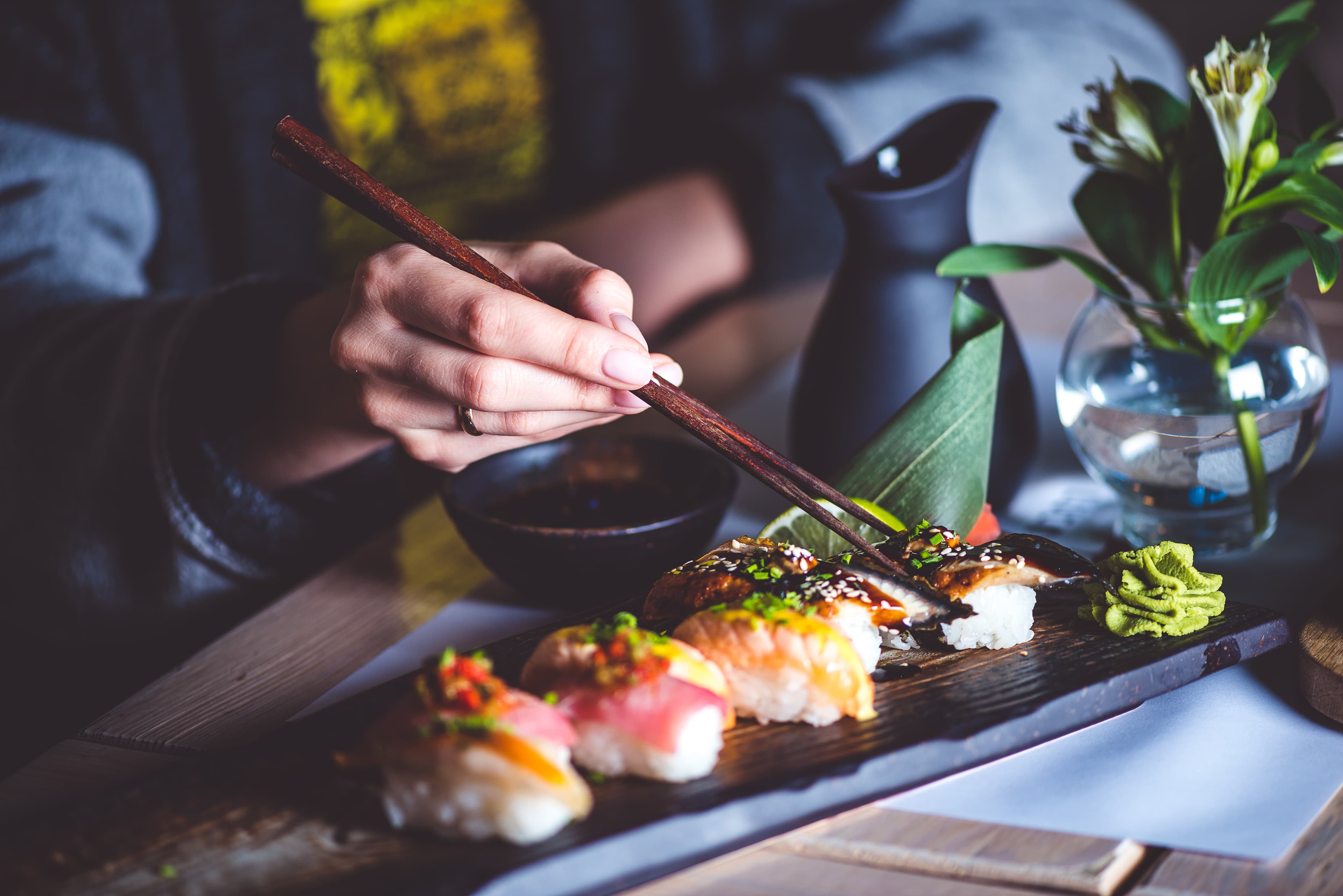 Chopsticks lifting nigiri from a wooden board of sushi.