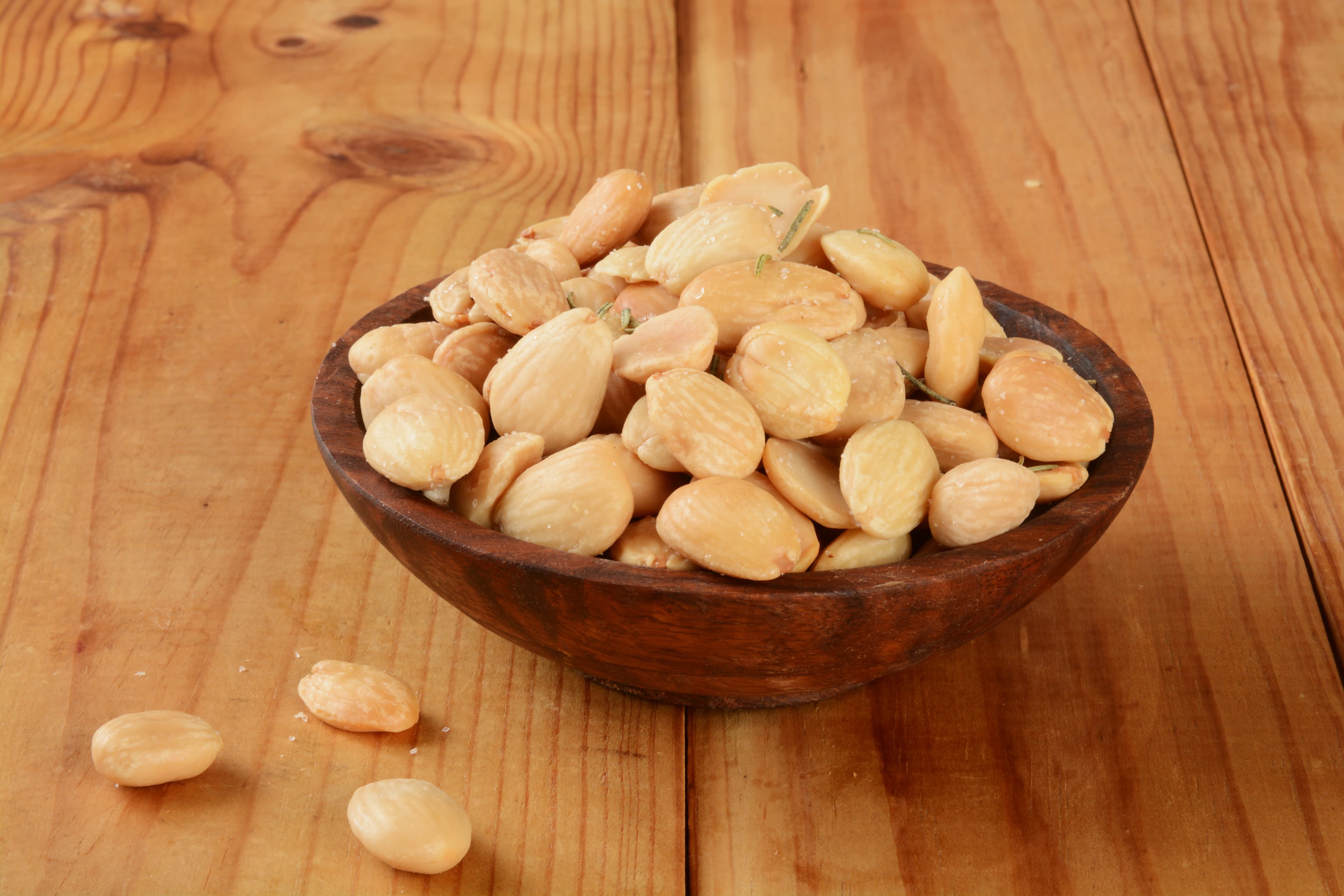 A wooden bowl of blanched almonds on a light wood table.
