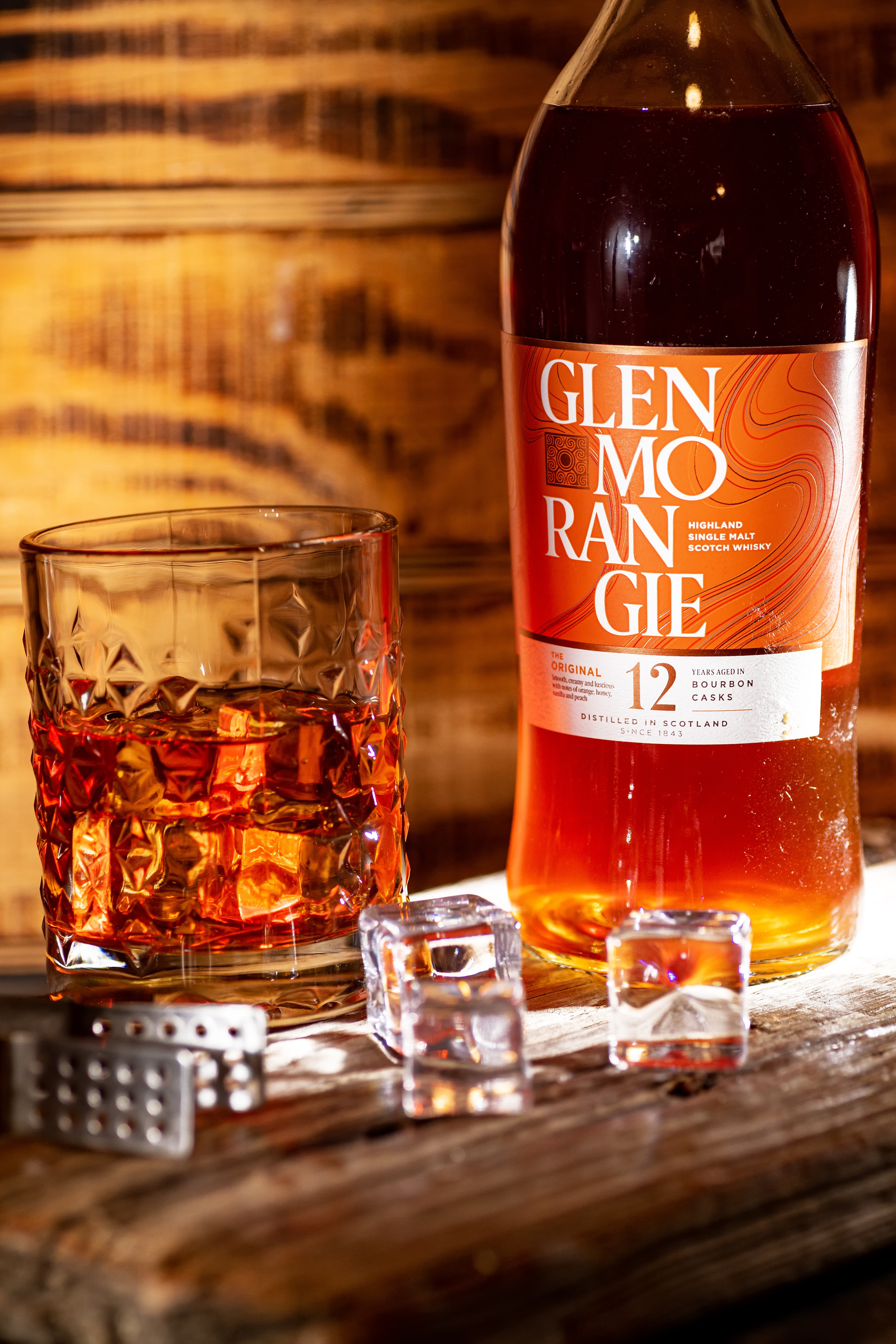 A Glenmorangie 12 bottle standing with a whisky glass and cooling stones.